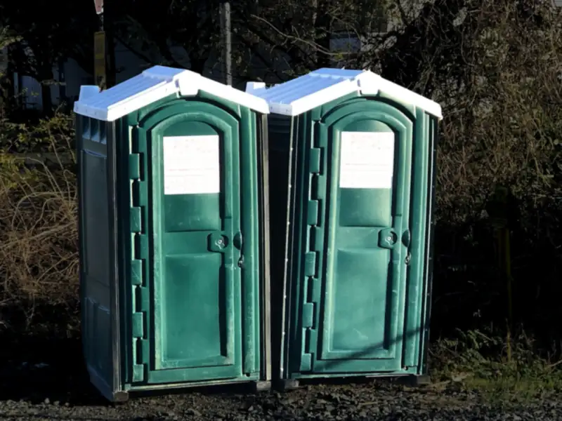 Two green portable toilets standing side by side outdoors (stock photo)